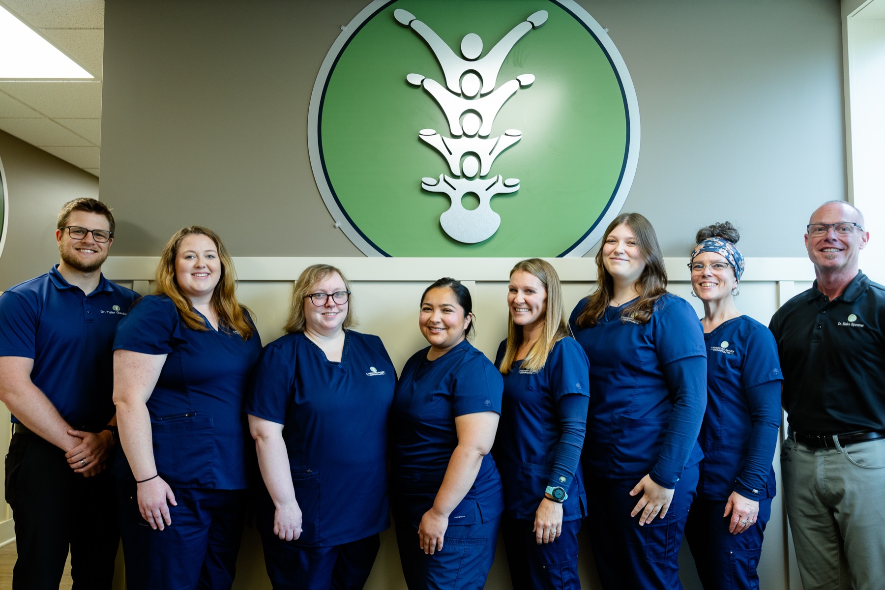 The full Lakeshore Family Chiropractic team in front of the practice emblem in Holland, MI